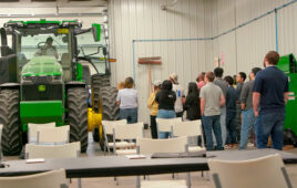 group of hackathon students gather around a john deere tractor.