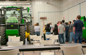 group of hackathon students gather around a john deere tractor.