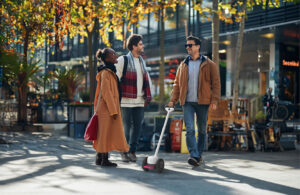 one man with Glide device talks to two friends, a man and a woman on the side, next to a cafe.