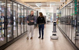 two workers walking through a store aisle next to a Tally robot.