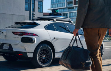 A person with a bag walking towards a Waymo robotaxi.